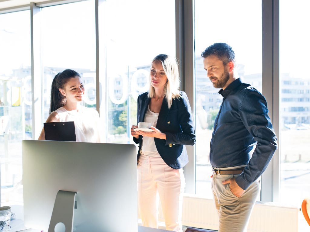 Tres profesionales de RRHH conversando frente a un monitor en una oficina moderna, simbolizando la transformación digital de recursos humanos y la colaboración estratégica.